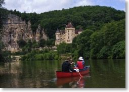 Young people canoing on the Dordogne River in France, past medieval castles and striking ancient cliff